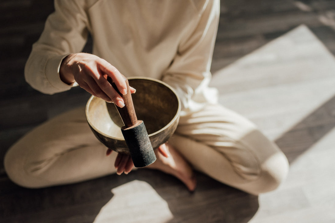 A seated person, who dressed in white, is playing a Himalayan singing bowl. 