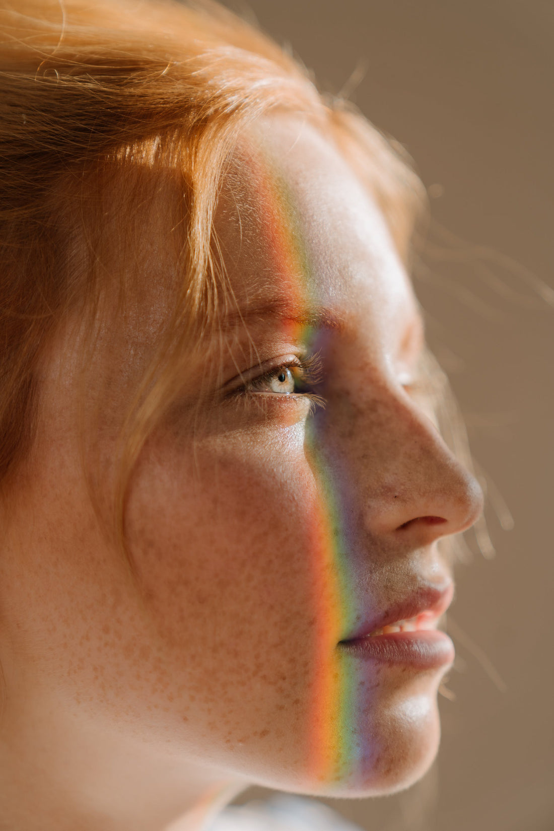 A red hair girl, with bluish green eyes looking to somewhere far away. A rainbow light reflected on her face.